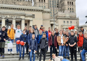 Grupa uczniów pozuje do zdjęcia na tle Pałacu Kultury i Nauki w Warszawie