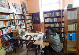 Wnętrze biblioteki szkolnej. Uczniowie przygotowują się do lekcji, korzystając z zasobów biblioteki.